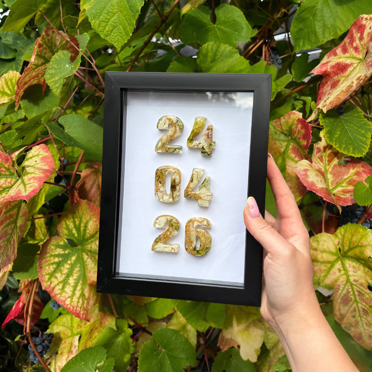 Framed numbers held by a hand against a leafy background