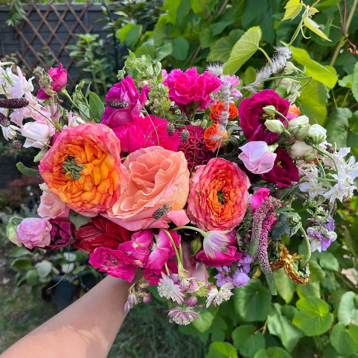 Bouquet of colorful flowers held by a person with greenery in the background