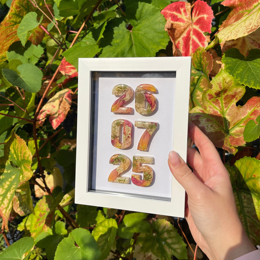Framed artwork with colorful numbers held by a hand among green leaves