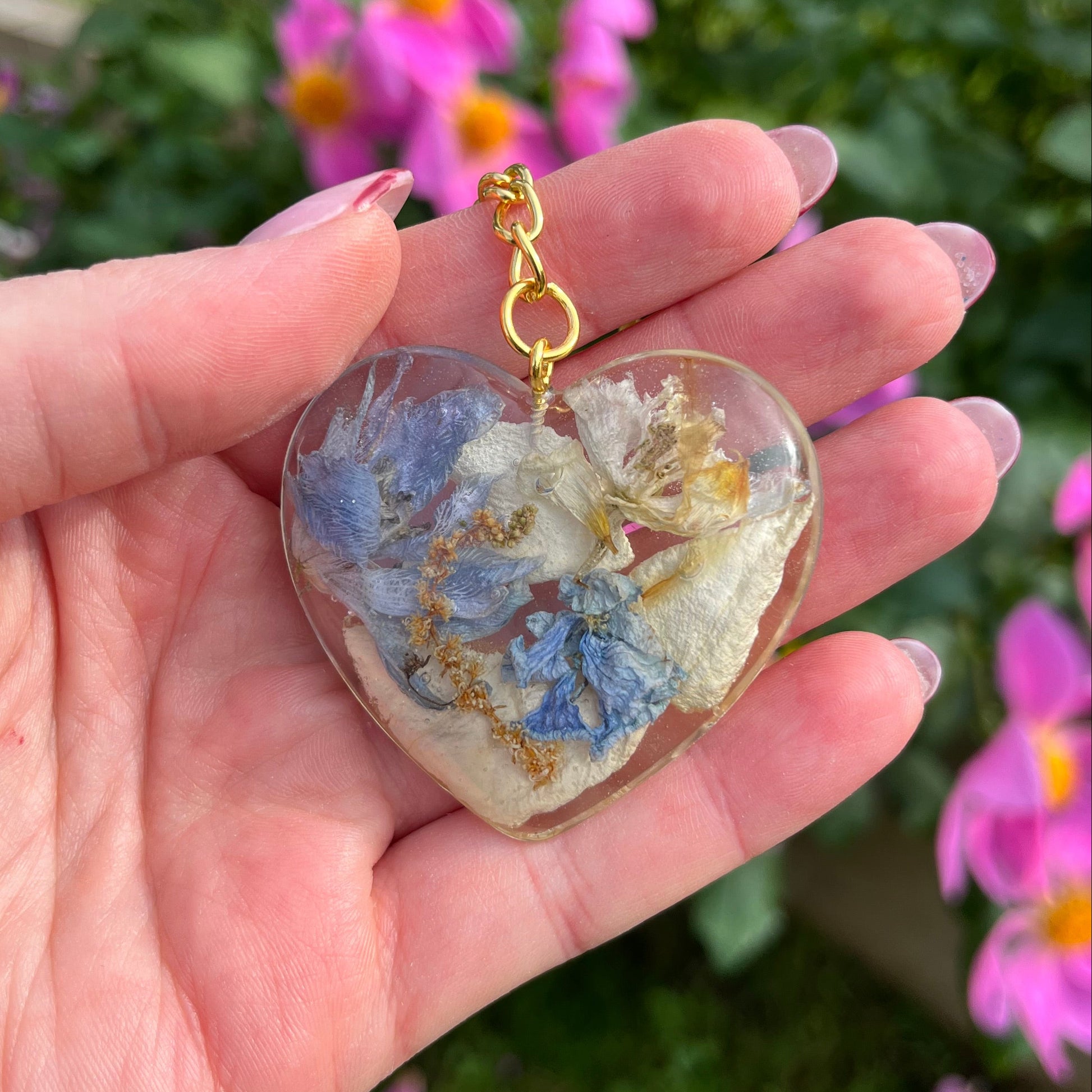 Heart-shaped pendant with floral design held in a hand against a blurred floral background