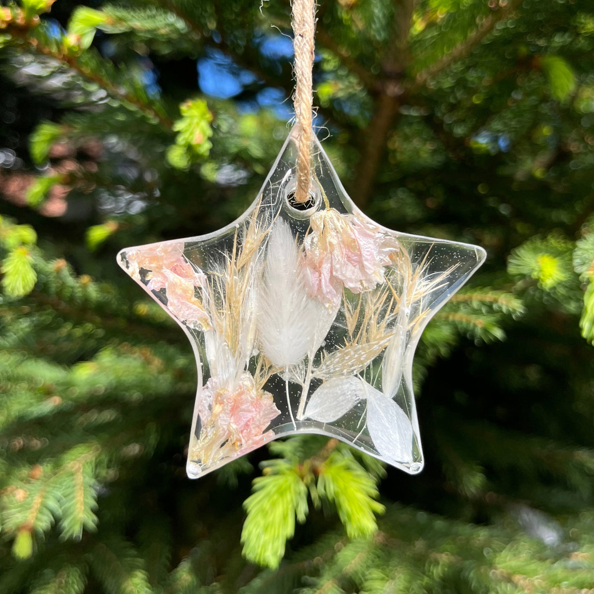 Star-shaped ornament with floral design on a string against a green tree background